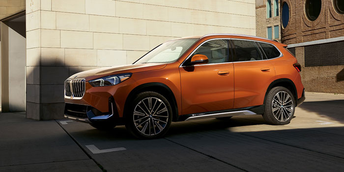 2025 BMW X1: side view, parked in urban area, stone wall and brick building in background.