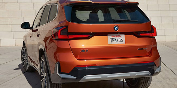 Orange BMW X1: rear view, "X1" badging, license plate, parked by stone wall.