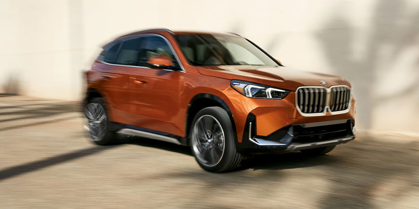 2025 BMW X1: front view, in motion on road, blurred background with shadow patterns.