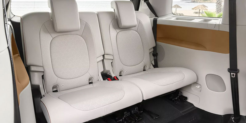 Light gray two-seat bench in a 2025 Volkswagen ID. Buzz’s interior, with beige trim; beach view visible through the window.