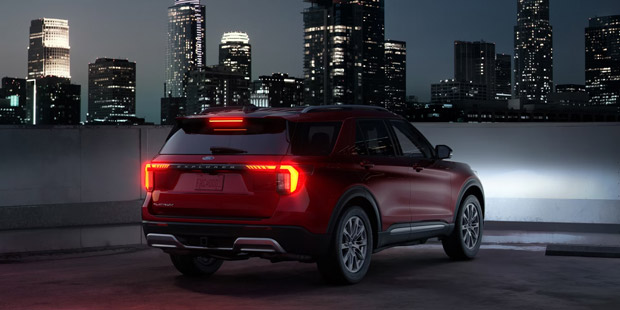 A three-quarters rear view of a 2026 Ford Explorer SUV with the taillamps illuminated
