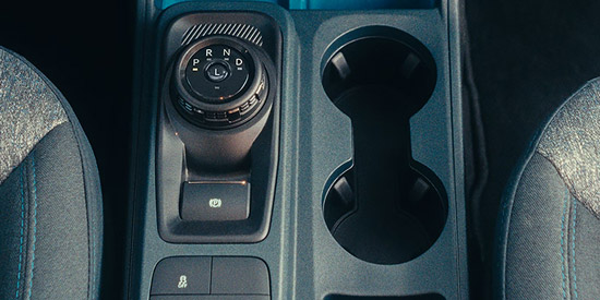A close-up of the center console of the 2026 Ford Maverick, showing cup holders and a driving mode selector knob