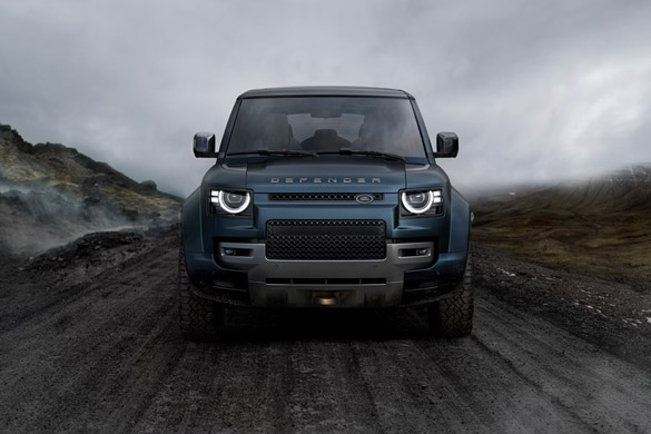 Front view of a blue Land Rover Defender on a rugged mountain road under cloudy skies