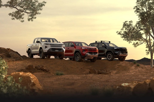 Three 2025 HiLux double-cab utes sit parked in a dirt clearing at golden hour. The first has Glacier White paint, the middle one is Feverish Red and the end one is As
