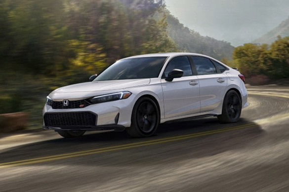 A white Honda Civic Si sedan with black wheels is captured in motion on a winding mountain road, with motion blur emphasizing its dynamic performance.