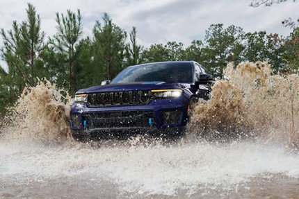 A blue 2025 Jeep Grand Cherokee Trailhawk 4xe is wading through water