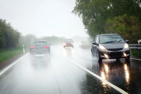 Cars driving with low beam headlights and fog lights on in heavy rain
