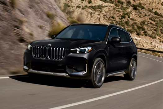 Shot of the 2026 BMW X1 xDrive28i SUV driving on a curvy road in a mountainous setting