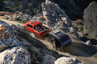 2026 Nissan Frontier in red loaded with cargo and pulling a trailer, on a rocky creekbed