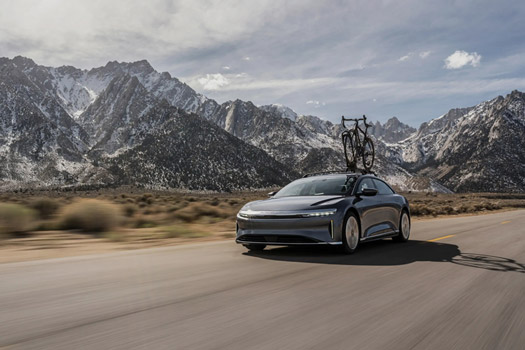Lucid Air with bicycle on roof rack driving on open road